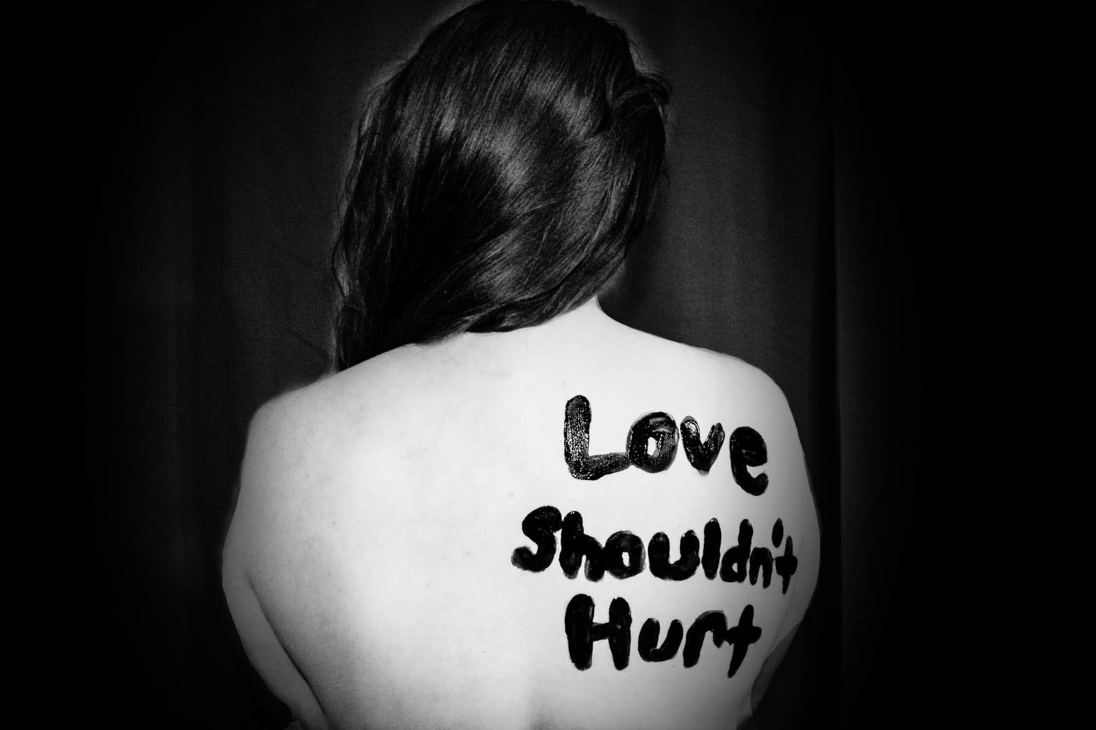 black and white photo of a woman's bare back with the words 'love shouldn't hurt' written on the shoulder